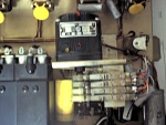 The black gear motor is the clock's timebase. It runs synchronously with the 60 hz line frequency, and is geared to 12 rpm. The four leaf switches on cams trigger in sequence every 5 seconds, to momentarily blank the display, enable the roll-over between the stepper relays, advance the 5-second relay, and finally, re-enable the display. The small relay to the motor's right is latched in momentarily by one of the leaf switches and the 5-second contacts to enable roll-over when the 5-second digit is rolling from 5 to 0.